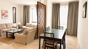 A modern living room with a sofa set, a glass-top dining table, and a decorative partition. - WAY RESDINCE (Jeddah)