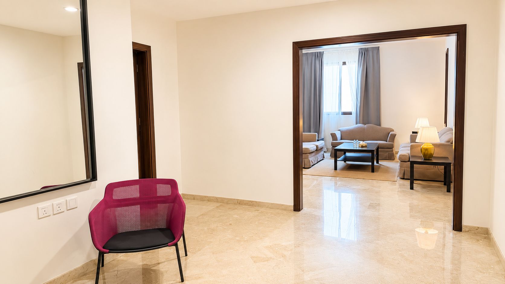 Habitación de hotel con un espejo grande, una silla rosa, un sofá, una mesa de centro y una lámpara.