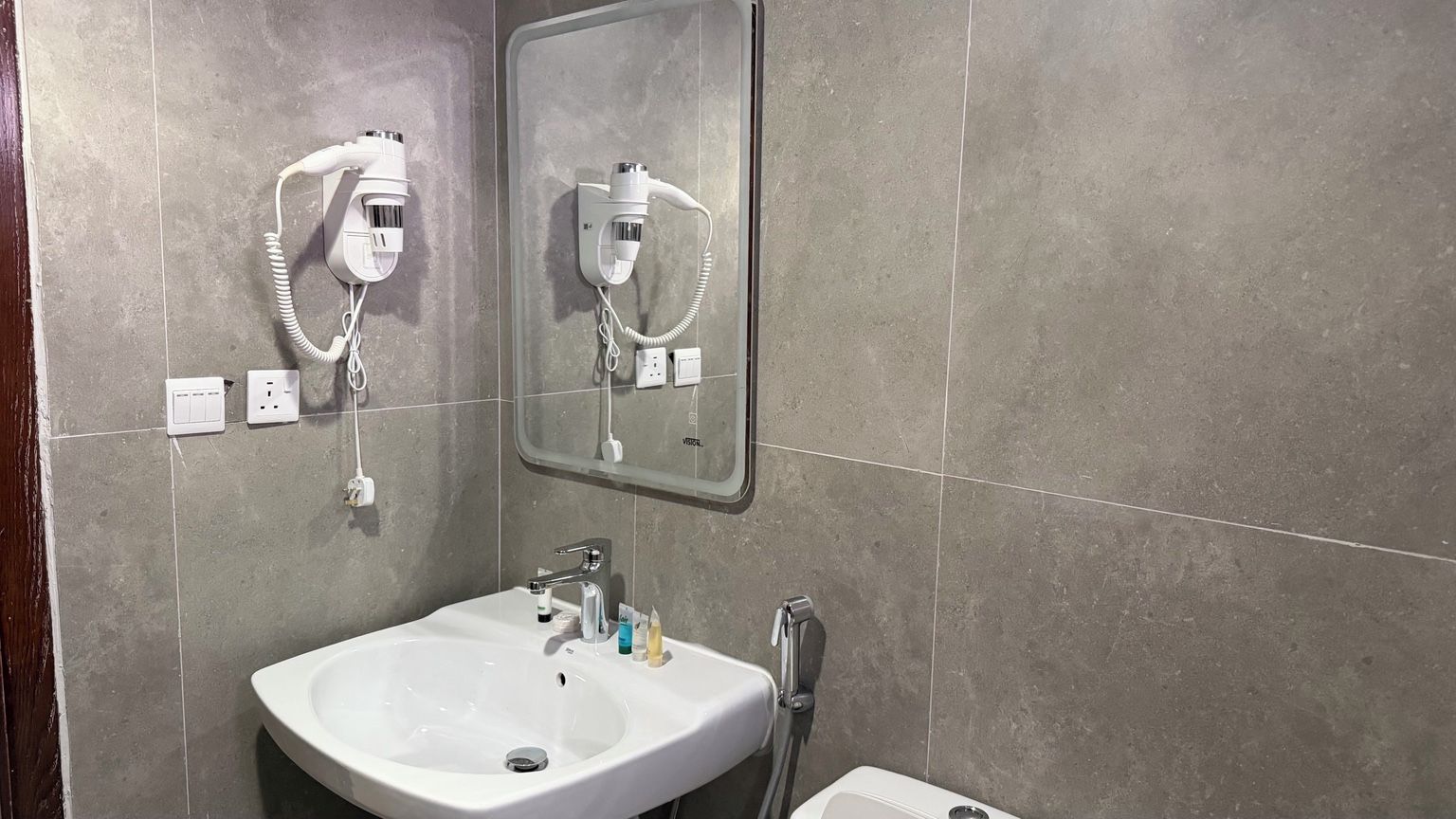 Un baño con un lavamanos blanco, un espejo y dos secadores de pelo fijados en la pared.
