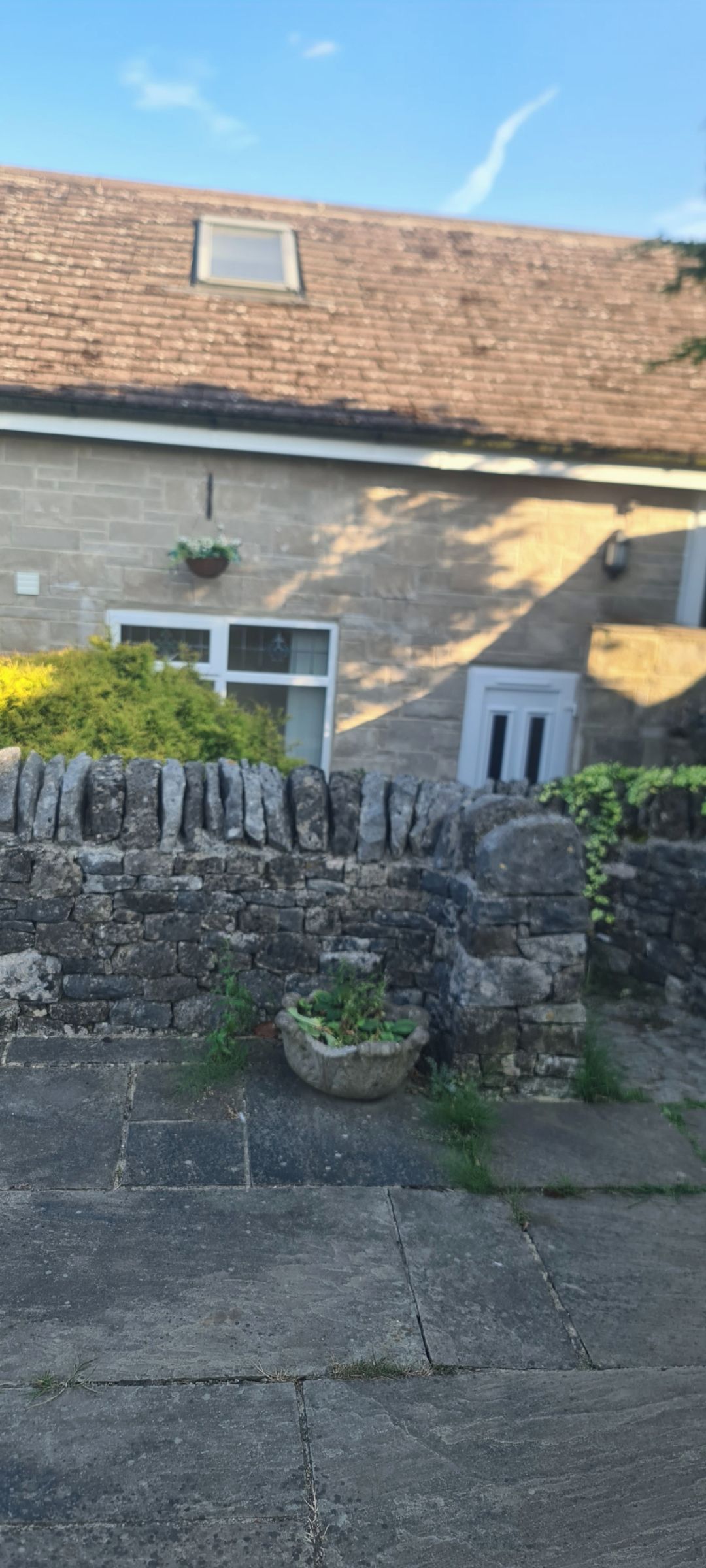 A stone wall, a concrete pathway, and a building with a tiled roof.