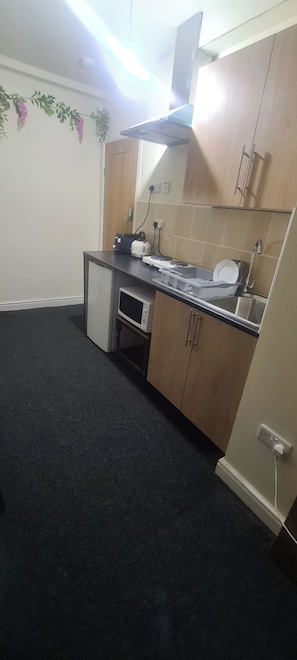 A compact kitchen with a microwave, kettle, and sink.