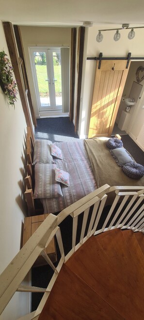 Ein Schlafzimmer mit einem Bett, Kissen, einem hölzernen Kopfteil, einem Fenster und einer Tür, die auf einen Balkon führt.