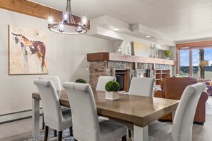 A modern dining area with a stone fireplace, a chandelier, and a view of the outdoors. - Eagle’s Rest – Your Mountain Getaway (Steamboat Springs)