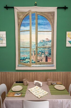 A dining area with a table set for two, a window with a view of a landscape, and a green wall. - Addu' Me Apartment with Balcony, Wi-Fi, and Air Conditioning (Napoli)