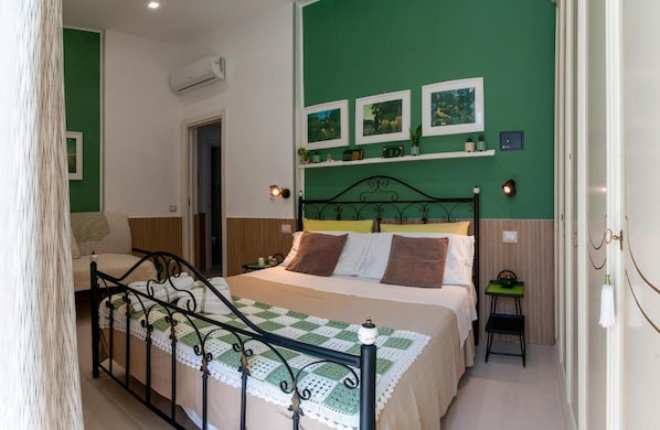 A bedroom with a bed, a bedside table, a chair, a green wall with pictures, and a door. - Addu' Me Apartment with Balcony, Wi-Fi, and Air Conditioning (Napoli)