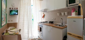 A compact kitchen with a stove, sink, and refrigerator. There is a dining area with a table and chairs. - Addu' Me Apartment with Balcony, Wi-Fi, and Air Conditioning (Napoli)