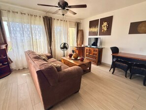 A living room with a sofa, a coffee table, a TV, and a fan. - 1-Bedroom Apartment in Pelican Key with Shared Pool & Balcony (Koolbaai)