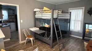 Un espacio habitable compacto con literas, kitchenette, comedor y ventana con cortinas.