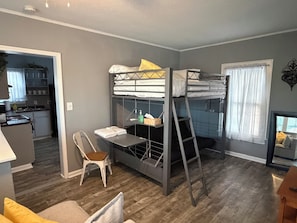 Ett kompakt bostadsutrymme med våningssängar, ett litet kök, en matplats och ett fönster med gardiner.