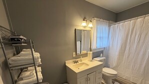 Un baño con lavabo, espejo, inodoro y un perchero con toallas dobladas.