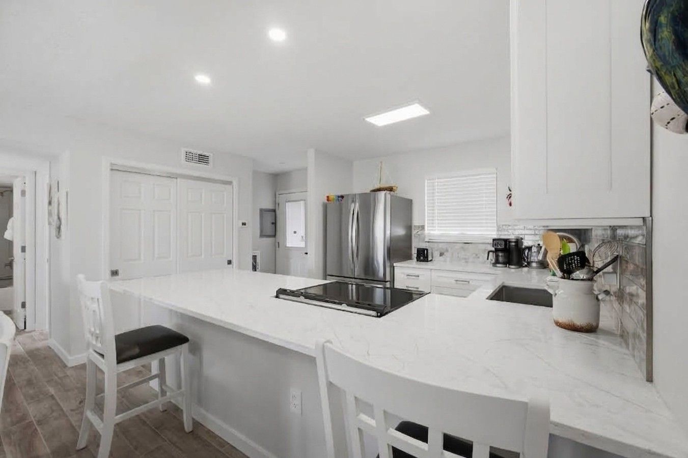 A modern kitchen with white cabinetry, stainless steel appliances, and a marble countertop.
