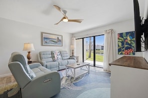 A living room with a sofa, armchairs, a coffee table, a ceiling fan, and a painting. - Runaway Bay 2BR|Steps to Beach + Heated pool/gym (Bradenton Beach)