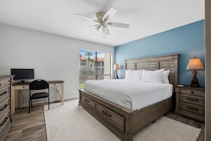 A bedroom with a bed, a desk, a chair, a ceiling fan, and a window with blinds. - Runaway Bay 2BR|Steps to Beach + Heated pool/gym (Bradenton Beach)