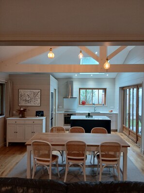 A modern kitchen with a central island, wooden dining table, and wicker chairs. - Lachanau Cabin: Relaxation and Fun with a Covered Terrace and Walkways Near the Lake (Hourtin)