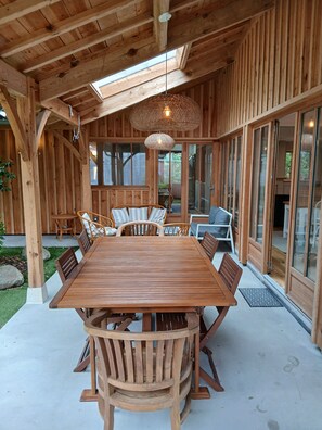 A wooden dining area with a large table and chairs, a hanging light fixture, and large windows. - Lachanau Cabin: Relaxation and Fun with a Covered Terrace and Walkways Near the Lake (Hourtin)