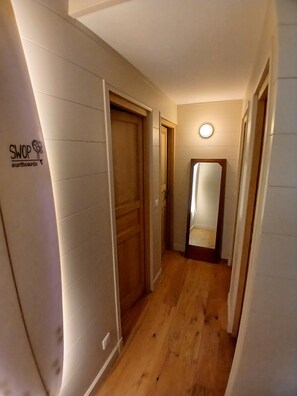 A hallway with wooden flooring, a closed door, and a mirror on the wall. - Lachanau Cabin: Relaxation and Fun with a Covered Terrace and Walkways Near the Lake (Hourtin)