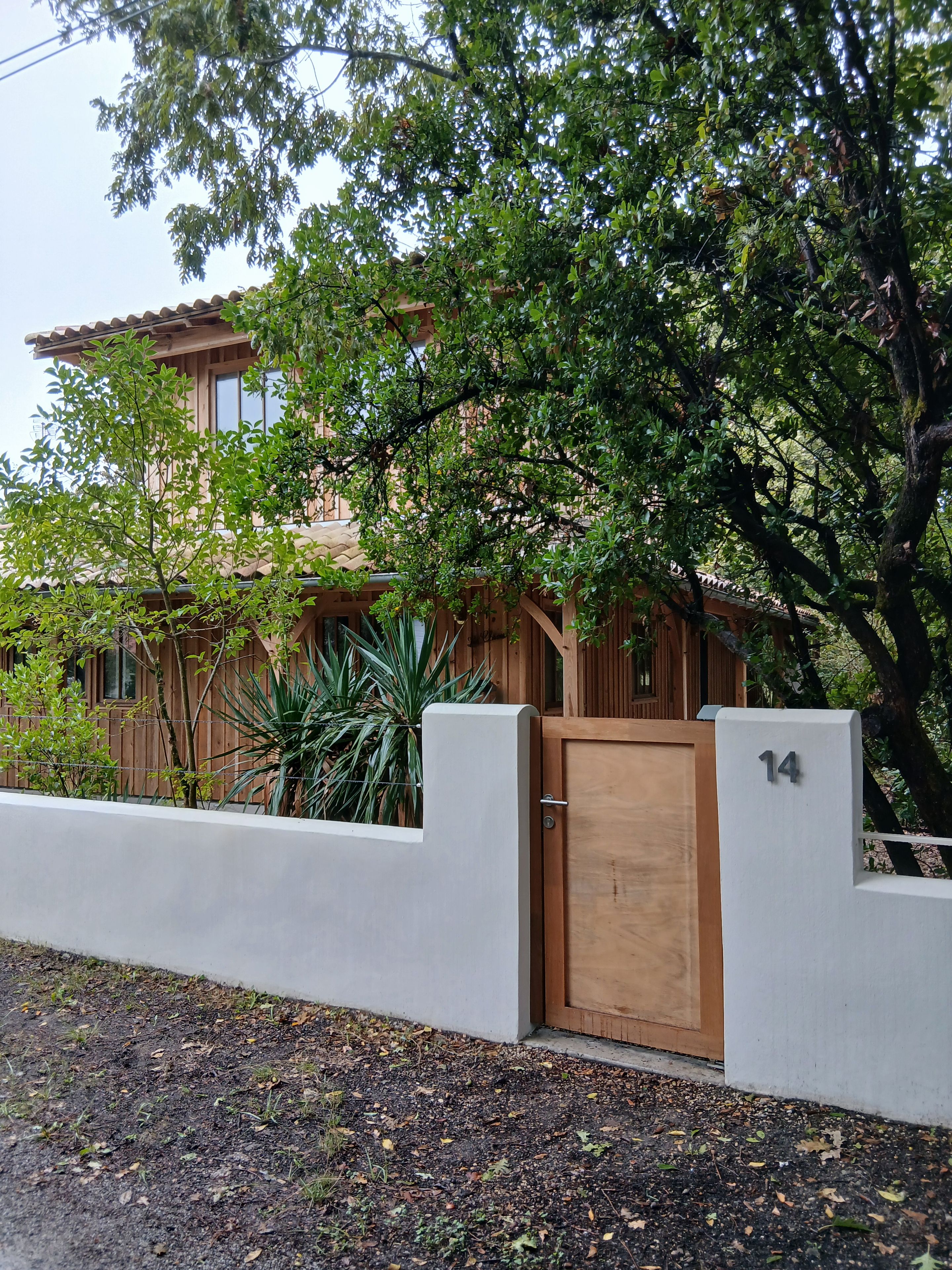 A residential building with a wooden gate, number 14, and a well-maintained garden with various plants.