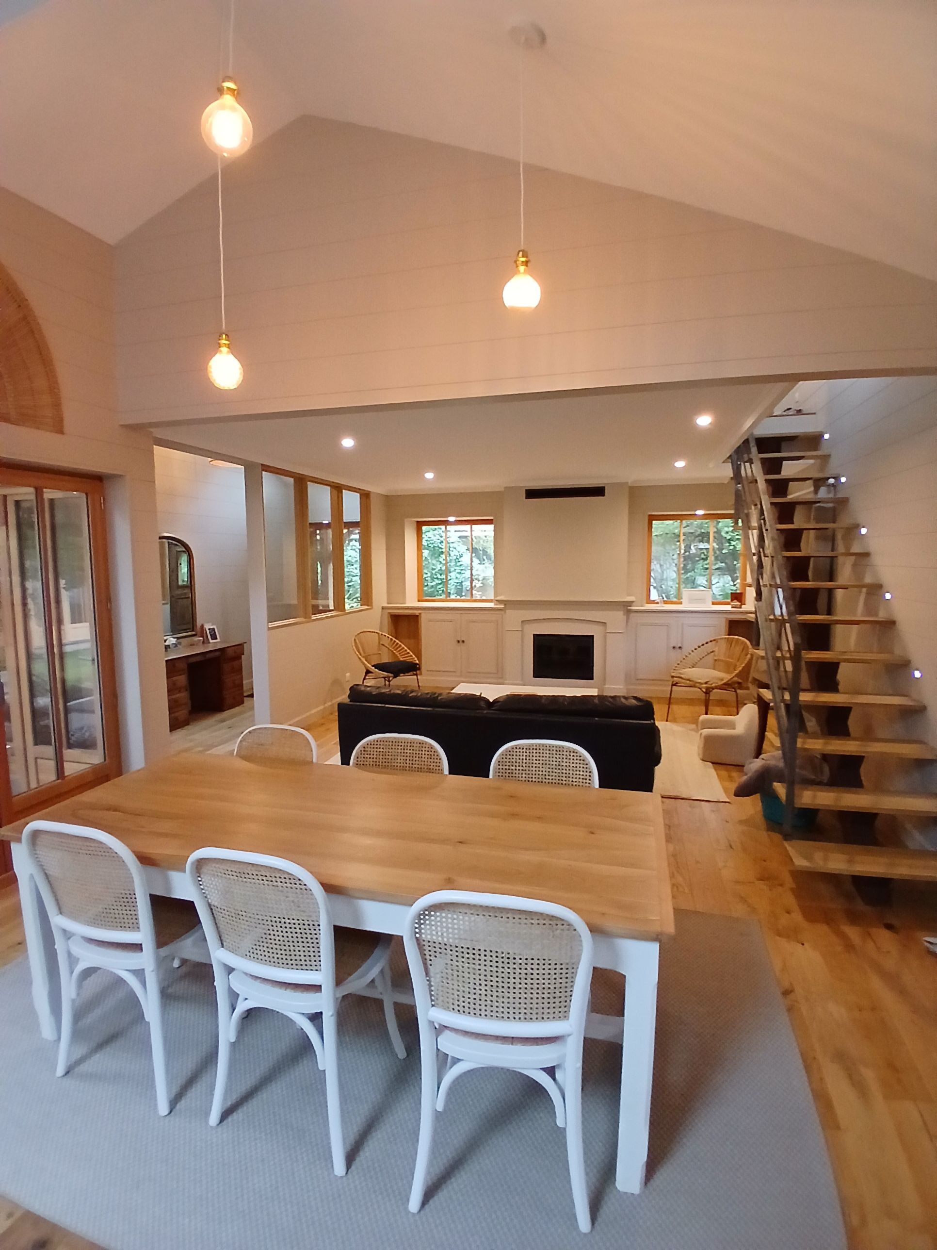 Una cocina moderna con zona de comedor, escalera de madera y amplios ventanales.
