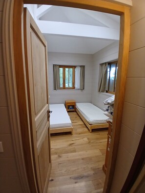 A compact room with two single beds, a small wooden nightstand, and a window with curtains. - Lachanau Cabin: Relaxation and Fun with a Covered Terrace and Walkways Near the Lake (Hourtin)