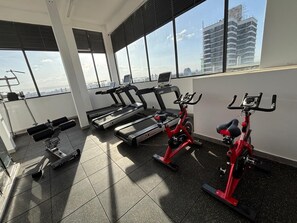 Een sportschool met loopbanden, een elliptische trainer en een hometrainer, met grote ramen met uitzicht op de stad.