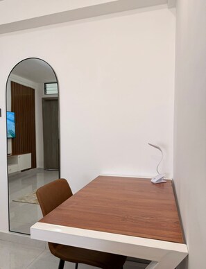 Een moderne eethoek met een houten tafel en stoelen, een witte muur en een spiegel die de ruimte weerkaatst.