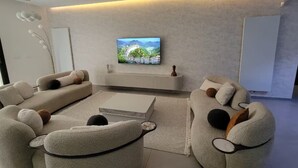 Een moderne woonkamer met een flatscreen televisie aan de muur, een zithoek en een salontafel.