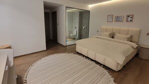 Een moderne slaapkamer met een groot bed, een douchecabine van glas en een rond vloerkleed.