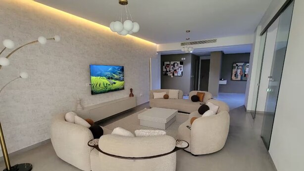 Een moderne woonkamer met een hoekbank, een flatscreen televisie en een vloerlamp.