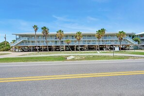 A multi-story hotel with a flat roof, outdoor seating area, and palm trees. - The Surf Shack | Gulf Shores Getaway (Gulf Shores)