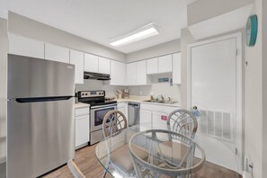 A modern kitchen with white cabinetry, stainless steel appliances, and a glass dining table. - The Surf Shack | Gulf Shores Getaway (Gulf Shores)