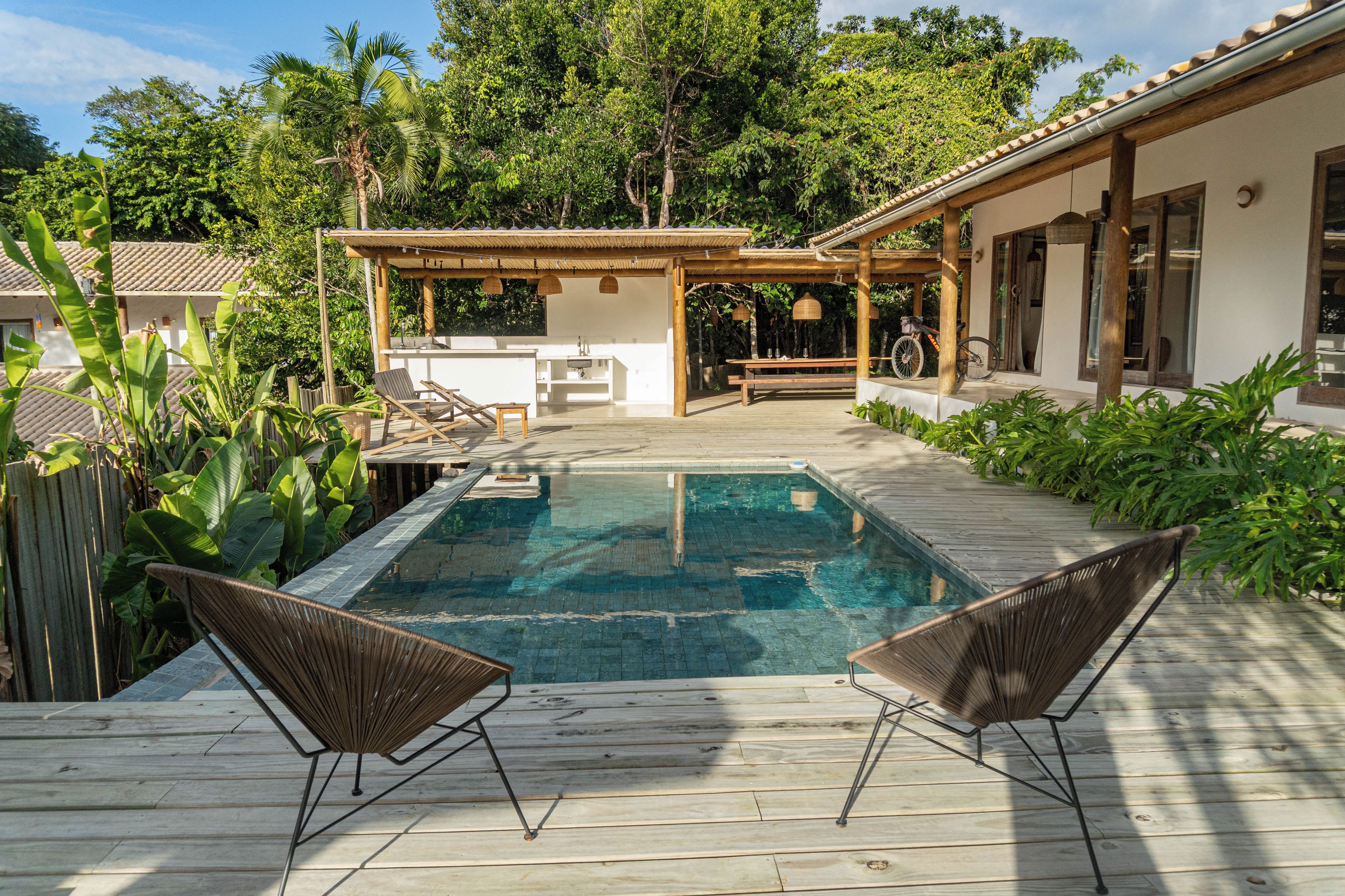 A swimming pool with two lounge chairs, a wooden deck, and a covered outdoor area with a table and chairs.