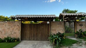 Une entrée fermée par un portail, surmontée d’un toit en tuiles, avec un mur en pierre et une clôture en bois.