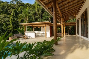 Ein überdachter Außenbereich mit Pool, Holzmöbeln und üppigem Grün.