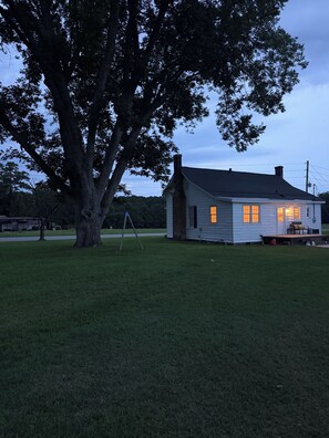 A house with a large tree in front, a lawn, and a porch with outdoor furniture.