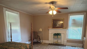 A bedroom with a bed, a chair, a fireplace, and a ceiling fan.