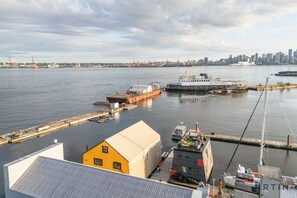 Une vue sur le front de mer, avec un grand bateau blanc amarré à un quai, un bâtiment jaune et, au loin, le profil de la ville.