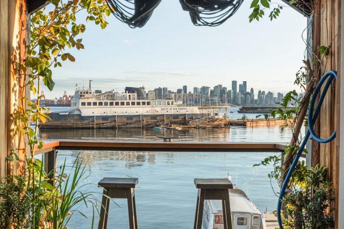 Blick vom Balkon auf einen Fluss mit einer großen Fähre und einer Stadtansicht im Hintergrund.