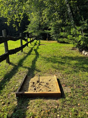 A fenced outdoor area with a sandbox and a wooden bench. - Romantic Cottage On the Lake (Alcove)