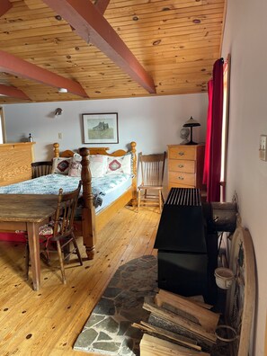 A room with a bed, wooden furniture, a piano, and a stone floor. - Romantic Cottage On the Lake (Alcove)