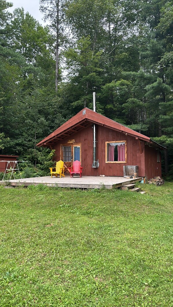Punaisella katolla varustettu puinen mökki, jossa on savupiippu ja kuisti, ja kuistilla on kaksi Adirondack-tyylistä puutarhatuolia.