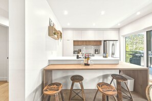A modern kitchen with white cabinets, a wooden countertop, and three stools with branding.