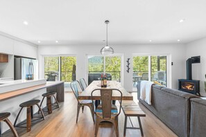 A modern kitchen with a dining area, large windows, and a wood-burning stove. - Spa-Aventure | Massif du Sud (Saint-Philémon)