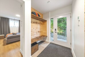 A modern interior with a wooden bench, a grey sofa, and a door leading to a natural outdoor area. - Spa-Aventure | Massif du Sud (Saint-Philémon)