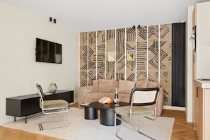 Ein modernes Wohnzimmer mit einer Couch, zwei Sesseln, einem Couchtisch, einem Fernseher und einer Wandablage mit Muster.