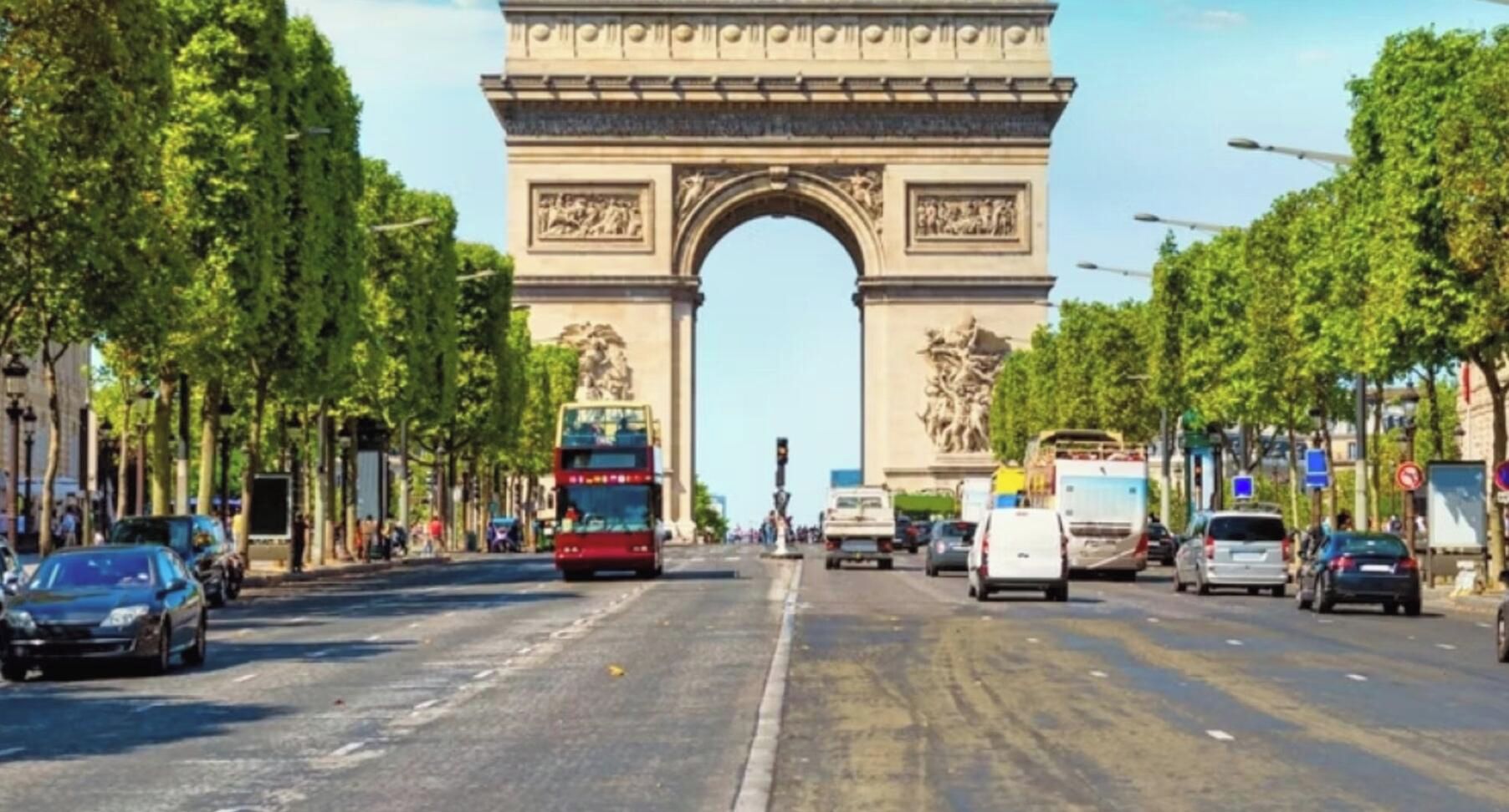 A street with a large historical archway, vehicles, and trees lining the road.