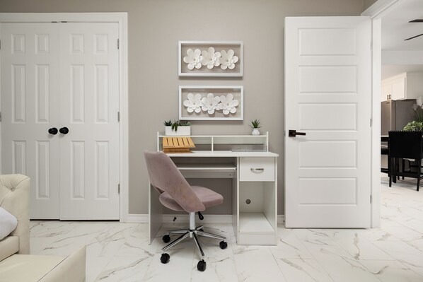 Un espacio de oficina moderno con un escritorio blanco, una silla de oficina rosa y dos adornos florales enmarcados en la pared.