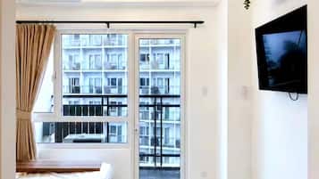 Une chambre à coucher moderne, avec un lit, un téléviseur fixé au mur, un luminaire au plafond et une fenêtre avec des rideaux.