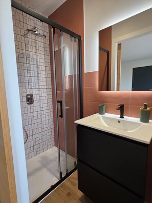 Een badkamer met een douche, een wastafel en een spiegel.