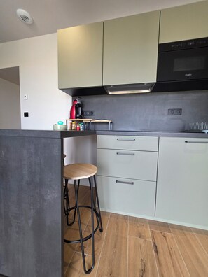 Een moderne keuken met een ingebouwde magnetron, een roestvrijstalen afzuigkap en een klein barretje met krukken.