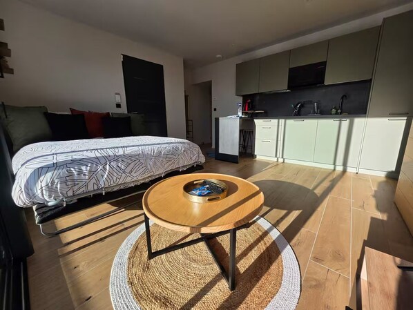 Een moderne slaapkamer met een bed, een ronde houten tafel en een keukenhoek met kasten en een aanrecht.